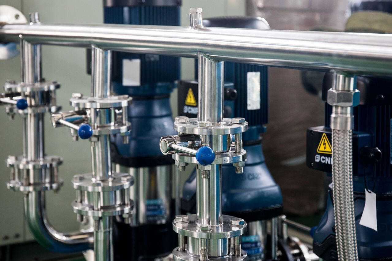 Close-up of industrial machinery featuring stainless steel piping in a factory setting. Stainless steel piping in a factory setting.